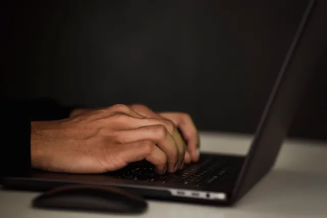 Hands typing on a laptop keyboard in a dimly lit workspace