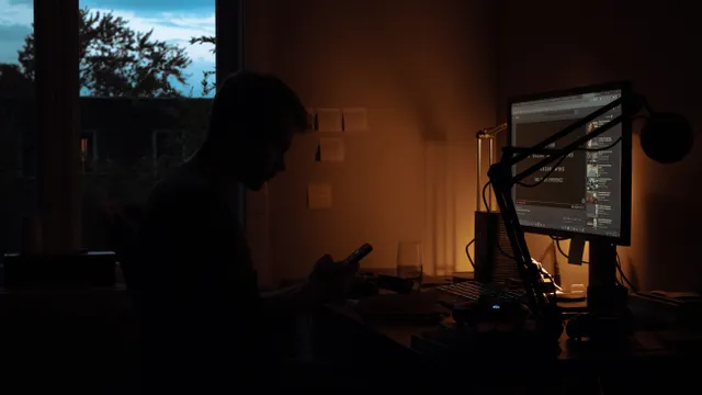 Person working in a dark room lit by computer screens