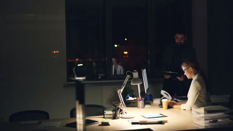 Two professionals working late at a desk, reviewing data on their screens